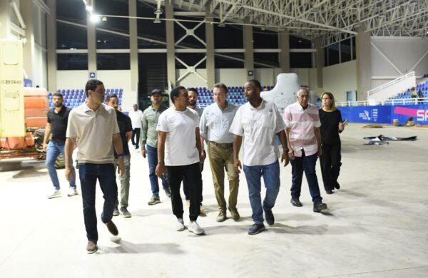 A una semana del inicio de los Juegos Centroamericanos y del Caribe Santo Domingo 2026, autoridades del Gobierno, del Comité Organizador y de Centro Caribe Sports realizaron un recorrido por las principales instalaciones deportivas para verificar el avance de las obras y los trabajos finales de acondicionamiento de los escenarios que recibirán a miles de atletas de la región. Durante la inspección, el ministro de Obras Públicas y Comunicaciones, Eduardo Estrella, afirmó que la institución mantiene un seguimiento permanente a las intervenciones en el Distrito Nacional, Santo Domingo, Santiago y otras provincias sedes, con el objetivo de garantizar el éxito del evento. Por su parte, el ministro de Vivienda y Edificaciones, Víctor “Ito” Bisonó, destacó el trabajo conjunto entre el MIVED, Obras Públicas y el Comité Organizador para entregar instalaciones deportivas y espacios públicos en condiciones óptimas, resaltando que las mejoras dejarán un legado permanente para la población. El presidente del Comité Organizador, José Monegro, expresó que la coordinación entre las instituciones permitirá mostrar la mejor imagen del país durante la edición del centenario de los Juegos, que reunirá la mayor cantidad de deportes, atletas e instalaciones en la historia del certamen regional. En tanto, el presidente de Centro Caribe Sports, Luis Mejía Oviedo, valoró el compromiso de las autoridades y señaló que las obras también han beneficiado a las comunidades cercanas mediante el asfaltado de calles, embellecimiento de edificios, construcción de verjas, ampliación de estacionamientos y preservación de áreas verdes. Mejía agregó que dirigentes deportivos internacionales que ya han visitado la Villa Centroamericana y los escenarios de competencia han destacado el nivel de las instalaciones y el avance de la organización, incluyendo el montaje de equipamientos especializados para disciplinas como la gimnasia. Las autoridades coincidieron en que los Juegos Centroamericanos y del Caribe Santo Domingo 2026 dejarán un importante legado deportivo y social para el país, al tiempo que exhortaron a la población a respaldar a la delegación dominicana y asistir a las competencias.