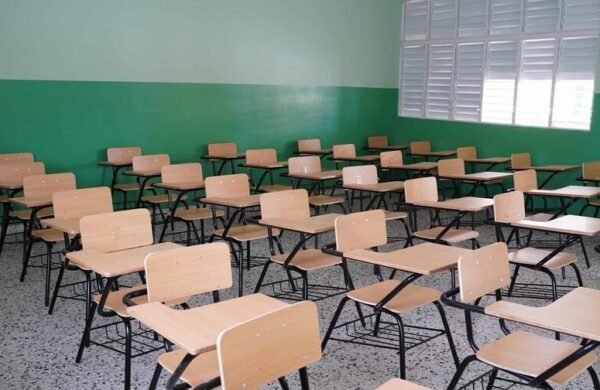 A menos de un mes del inicio oficial del año escolar 2026-2027, programado por el Ministerio de Educación (Minerd) para el lunes 24 de agosto, la Asociación Dominicana de Profesores (ADP) advirtió que el sistema educativo nacional enfrenta un déficit de 28 mil aulas, más de 3 mil docentes y alrededor de 600 centros educativos con problemas de infraestructura. Déficit estructural El dirigente magisterial Sixto Gabín, coordinador del Espacio Magisterial Narciso González, afirmó que el Minerd no ha aprovechado el receso escolar para corregir las debilidades con las que concluyó el año lectivo 2025-2026. “Históricamente espera a que inicie un año escolar con las mismas problemáticas con que terminó el anterior”, expresó. Según sus estimaciones, el déficit de aulas impediría que más de 200 mil estudiantes encuentren cupo para recibir docencia al inicio del nuevo período escolar. Centros deteriorados Gabín aseguró que más de 600 planteles permanecen en condiciones de deterioro y no fueron intervenidos durante las vacaciones escolares, lo que amenaza el normal desarrollo de la docencia. Falta de personal El sistema educativo registra una carencia superior a 3 mil docentes, además de conserjes, guardianes y personal de apoyo indispensable para el funcionamiento de los planteles, especialmente en la Jornada Escolar Extendida. Agregó que todavía existen maestros que aprobaron los concursos de oposición realizados en 2023 y 2024 y permanecen a la espera de ser nombrados por el Ministerio de Educación. Recursos pedagógicos insuficientes El dirigente señaló que los libros de texto para el año escolar 2026-2027 aún no han llegado a numerosos centros educativos y que alrededor del 70 % de las escuelas carece de laboratorios de ciencias, limitando el proceso de enseñanza y aprendizaje. También cuestionó el alcance del operativo de distribución de útiles escolares del Inabie, al considerar que la cantidad de uniformes y materiales entregados resulta insuficiente para cubrir la demanda de las familias. Formación integral afectada Gabín advirtió que la Jornada Escolar Extendida iniciará con déficit de monitores de artes, educación física y personal de apoyo, lo que afecta la formación integral de los estudiantes. Asimismo, criticó el proceso de evaluación del desempeño docente, al considerar que aún permanecen pendientes la aplicación de incentivos y la ejecución de la etapa complementaria que permita identificar fortalezas y debilidades del personal. Exhortación al Minerd Ante este panorama, la ADP exhortó al Ministerio de Educación a transparentar la situación del sistema educativo y adoptar medidas urgentes antes del 24 de agosto, fecha fijada para el inicio del año escolar, con el propósito de evitar dificultades en el regreso de millones de estudiantes a las aulas.