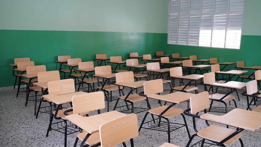 A menos de un mes del inicio oficial del año escolar 2026-2027, programado por el Ministerio de Educación (Minerd) para el lunes 24 de agosto, la Asociación Dominicana de Profesores (ADP) advirtió que el sistema educativo nacional enfrenta un déficit de 28 mil aulas, más de 3 mil docentes y alrededor de 600 centros educativos con problemas de infraestructura. Déficit estructural El dirigente magisterial Sixto Gabín, coordinador del Espacio Magisterial Narciso González, afirmó que el Minerd no ha aprovechado el receso escolar para corregir las debilidades con las que concluyó el año lectivo 2025-2026. “Históricamente espera a que inicie un año escolar con las mismas problemáticas con que terminó el anterior”, expresó. Según sus estimaciones, el déficit de aulas impediría que más de 200 mil estudiantes encuentren cupo para recibir docencia al inicio del nuevo período escolar. Centros deteriorados Gabín aseguró que más de 600 planteles permanecen en condiciones de deterioro y no fueron intervenidos durante las vacaciones escolares, lo que amenaza el normal desarrollo de la docencia. Falta de personal El sistema educativo registra una carencia superior a 3 mil docentes, además de conserjes, guardianes y personal de apoyo indispensable para el funcionamiento de los planteles, especialmente en la Jornada Escolar Extendida. Agregó que todavía existen maestros que aprobaron los concursos de oposición realizados en 2023 y 2024 y permanecen a la espera de ser nombrados por el Ministerio de Educación. Recursos pedagógicos insuficientes El dirigente señaló que los libros de texto para el año escolar 2026-2027 aún no han llegado a numerosos centros educativos y que alrededor del 70 % de las escuelas carece de laboratorios de ciencias, limitando el proceso de enseñanza y aprendizaje. También cuestionó el alcance del operativo de distribución de útiles escolares del Inabie, al considerar que la cantidad de uniformes y materiales entregados resulta insuficiente para cubrir la demanda de las familias. Formación integral afectada Gabín advirtió que la Jornada Escolar Extendida iniciará con déficit de monitores de artes, educación física y personal de apoyo, lo que afecta la formación integral de los estudiantes. Asimismo, criticó el proceso de evaluación del desempeño docente, al considerar que aún permanecen pendientes la aplicación de incentivos y la ejecución de la etapa complementaria que permita identificar fortalezas y debilidades del personal. Exhortación al Minerd Ante este panorama, la ADP exhortó al Ministerio de Educación a transparentar la situación del sistema educativo y adoptar medidas urgentes antes del 24 de agosto, fecha fijada para el inicio del año escolar, con el propósito de evitar dificultades en el regreso de millones de estudiantes a las aulas.