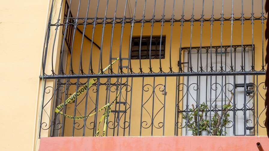 La Policía Nacional informó que los primeros resultados de la investigación sobre la muerte de Lucinda Emelinda Rodríguez Restituyo, de 68 años, y su hijo Óscar Gabriel Curiel Rodríguez, de 41, hallados sin vida en un apartamento del sector Bella Vista, en el Distrito Nacional, indican que ambos cuerpos no presentan signos de violencia. El vocero de la institución, Diego Pesqueira, explicó que se trata de un informe preliminar y que será el Instituto Nacional de Ciencias Forenses (Inacif) el organismo encargado de establecer oficialmente la causa de los fallecimientos, una vez concluyan las autopsias. Las investigaciones también revelan que los familiares de las víctimas creían que madre e hijo habían salido de la ciudad durante el fin de semana, luego de que Lucinda comunicara a otro de sus hijos, miembro de las Fuerzas Armadas, que realizarían un viaje. Mientras sus parientes pensaban que ambos estaban fuera, residentes del edificio comenzaron a percibir un fuerte hedor, que inicialmente atribuyeron a un animal muerto. Días después, las autoridades localizaron los cuerpos en avanzado estado de descomposición dentro del apartamento. Vecinos describieron a las víctimas como personas reservadas y tranquilas, con escaso contacto con los demás residentes, y señalaron que solían salir únicamente para pasear a su perro. La Policía informó que las investigaciones continúan y que han sido entrevistados familiares, vecinos y comerciantes de la zona, en espera de los resultados oficiales del Inacif que permitan esclarecer las circunstancias de ambas muertes.