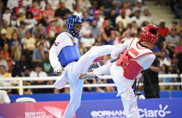El dominicano Wilfrido de la Cruz otorgó este domingo la tercera medalla de oro a la representación de la República Dominicana en los XXV Juegos Centroamericanos y del Caribe Santo Domingo 2026, al imponerse en la final de los -54 kilos masculino del torneo de taekwondo. Camino al título De la Cruz venció en la final al hondureño Derek Midence por 2-0, en un combate disputado en el Pabellón de Combates del Centro Olímpico Juan Pablo Duarte. Para llegar al desenlace, derrotó primero al guatemalteco Diego Reyes y en semifinal superó al mexicano Sebastián Echavarría, mostrando solidez en cada presentación. Debut en el Ciclo Olímpico El joven atleta debutó en competencias del Ciclo Olímpico, convirtiéndose en parte del relevo generacional que toma la antorcha del taekwondo dominicano. Su triunfo refuerza la presencia del país en una disciplina que históricamente ha dado medallas en eventos regionales y mundiales. Balance dominicano Con este resultado, la delegación dominicana suma tres oros en la justa regional, tras los conseguidos por las judocas Ana Rosa y Esmeralda Damiano. La jornada dominical también fue histórica: la República Dominicana alcanzó las mil medallas acumuladas en la historia de los Juegos Centroamericanos y del Caribe, cifra lograda gracias a los aportes recientes en judo, taekwondo y esquí náutico. Las mil medallas El país inició Santo Domingo 2026 con 993 preseas acumuladas. El sábado sumó cinco más y este domingo agregó dos bronces de Francesca Pigozzi en esquí náutico y el oro de De la Cruz, alcanzando la marca simbólica de las 1,000 medallas. Pigozzi se destacó en figuras femenino, con 1,870 puntos, detrás de las colombianas Daniela Verswyvel (oro, 7,310) y Martina Piedrahita (plata, 3,710). En salto femenino, volvió a subir al podio con 18.5 metros, en otra competencia dominada por Colombia.